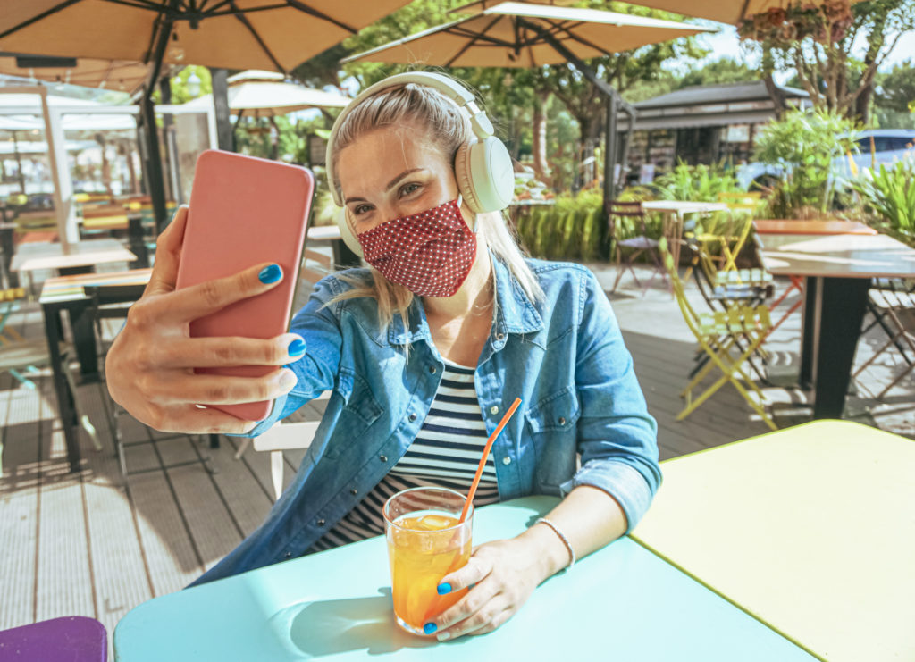 Girl in bar taking a selfie with a smartphone with her face mask on as a protection for coronavirus time.