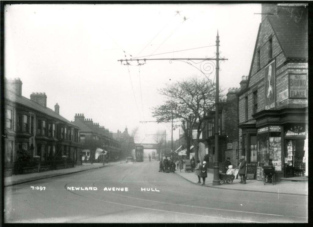 Black and white photo taken in 1922 taken from the bottom of Newland Avenue looking north. There are people pushing prams and shopping on the pavements. There is a tram on the tracks going north towards the bridge. Ornate posts hold the tramlines above the street.