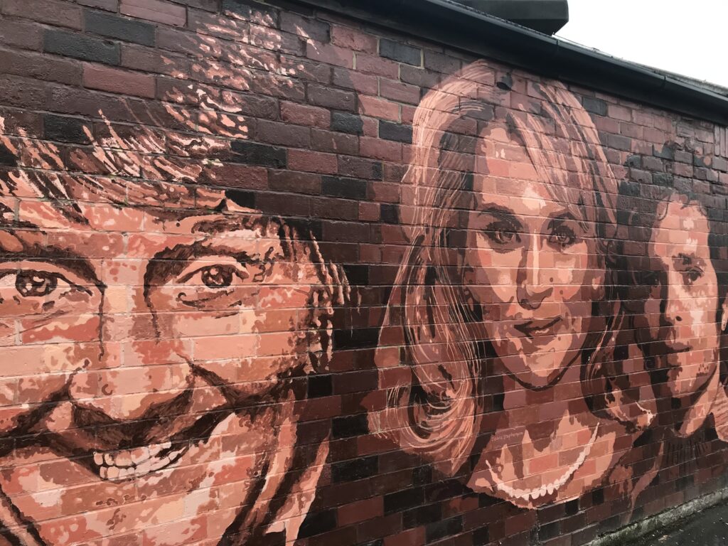 A mural of Hull-born celebrities painted in brown tones into a brick wall